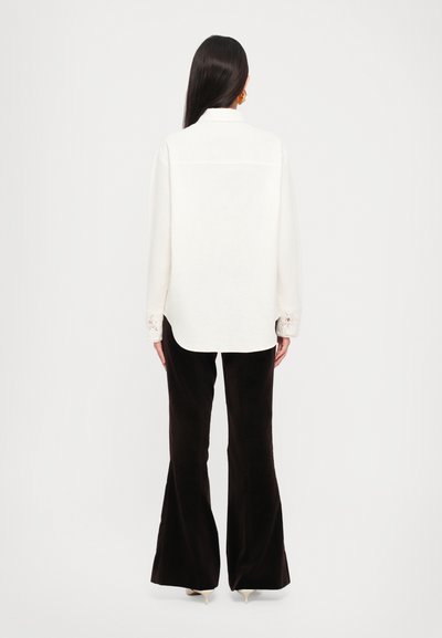 Long-sleeved white shirt with a collar and lace accents at the cuffs, paired with black flared pants and beige heeled shoes.