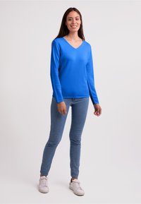 Maglione blu a V con maniche lunghe e texture liscia. Indossato con jeans skinny blu chiaro e sneakers bianche. Design semplice, senza motivi.