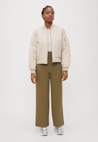 Beige bomber jacket with elastic cuffs, paired with wide-leg olive green pants featuring a ribbed texture. Silver sneakers complete the look.