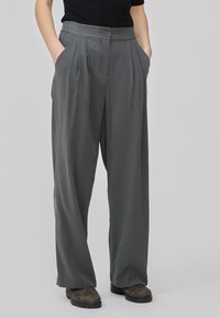 Pantalons plissés gris à taille haute, dotés de poches latérales et d'une fermeture à un bouton, fabriqués dans un matériau lisse et léger.
