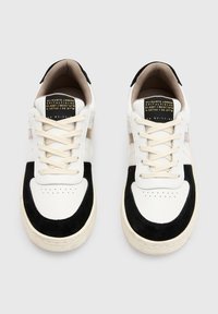 Bílé a černé tenisky s horní částí z kůže a semiše, kulatou špičkou, perforovanými detaily, plochými tkaničkami a kontrastními akcenty na patě.