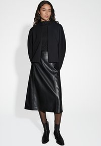 Cardigan en mélange de laine noir sur un col roulé côtelé noir, associé à une jupe midi en simili cuir noir et des bottes noires à mi-mollet.