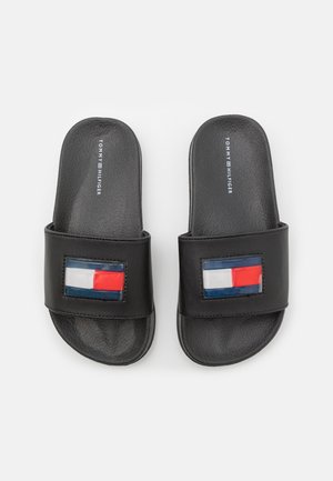 Sandalias negras tipo chancla de Tommy Hilfiger con parches de logo en rojo, blanco y azul en tiras anchas, plantillas texturizadas, sobre un fondo blanco.
