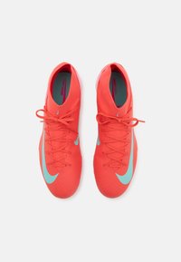 Lyse røde fodboldstøvler med tekstureret overdel, lyseblå Nike-swoosh, traditionelt snørebåndsdesign og polstret krave. Indeni har de en blød foring.