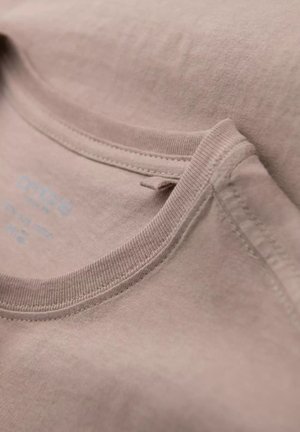 T-shirt rose clair avec un col rond, en tissu de coton doux, et des coutures visibles. L'étiquette est subtilement imprimée sur le tissu.