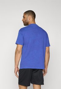 Camiseta de algodón azul de corte relajado, con mangas cortas y escote redondo. Combinada con pantalones cortos deportivos de malla negros.