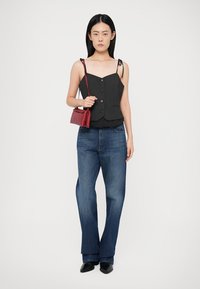 Schwarzes ärmelloses Oberteil mit Knöpfen, kombiniert mit lockeren blauen Jeans und einer kleinen roten Handtasche. Einfaches Design, glattes Material und minimale Details.