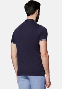 Granatowa koszulka polo o dopasowanym kroju, z krótkimi rękawami i białymi paskami przy kołnierzyku oraz rękawach. Urokowi dodaje logo marki umieszczone przy dekolcie.