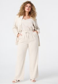 Hellbeige, gestreiftes Loungewear-Set mit einem lockeren Blazer, einem Tanktop und elastischen Hosen mit Taschen. Glatte Textur, lässige Passform.
