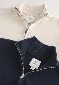Zwei gefaltete Half-Zip-Pullover, einer beige und einer navy, beide mit gerippten Kragen und silbernen Reißverschlüssen, mit NEXT-Markenetiketten.