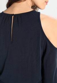 Námořnicky modrý top s odhalenými rameny z měkké látky, s průstřihem na zádech a jemnými sklady u výstřihu.