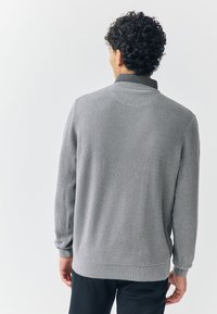 Grå ribbad tröja med krage, med långa ärmar och ett texturerat tyg. Bakifrån syns en enkel design och elastiska fållar.