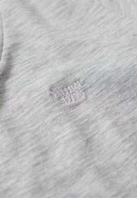 T-shirt en coton gris au toucher doux, arborant un logo brodé subtil "super dry" dans un gris légèrement plus foncé.