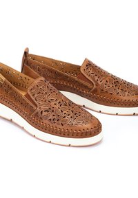 Brown leather slip-on shoes featuring intricate laser-cut floral patterns, a white rubber sole, and decorative stitching along the edges.