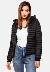 Zwarte gewatteerde jas met capuchon, voorzien van een ritssluiting en geribbelde boorden. Gedragen over een witte top en blauwe jeans, waarbij de textuur en pasvorm worden benadrukt.