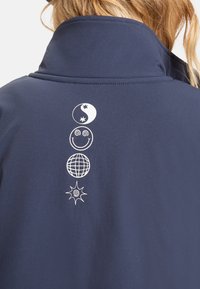 Navyblauwe jack met een gestructureerde afwerking. Heeft een hoge kraag en witte grafische symbolen die verticaal op de rug zijn gedrukt.