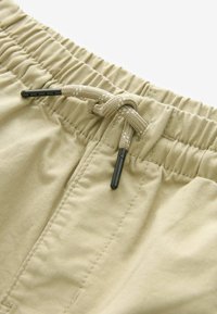 Beige elastiske shorts med en tekstureret stof, snor med sorte spidser og subtile stikninger langs taljen.