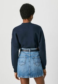 Marinblå sweatshirt med sänkt axel och rundad halsringning, tillsammans med en ljusblå denimminikjol med ett svart bälte och bakfickor.