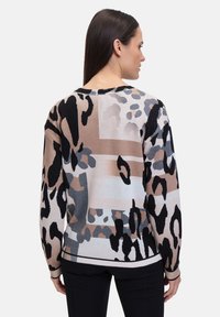 Knit sweater featuring a blend of leopard and abstract patterns in beige, black, and grey. Relaxed fit with ribbed cuffs and hem.
