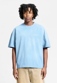 Light blue oversized cotton t-shirt with short sleeves and crew neckline, featuring a small white logo on the front.