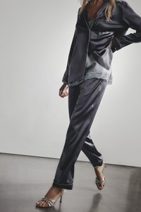 Marineblåt satin pyjamasæt med blondekant ved sømmen. Indeholder en skjorte med knapper og matchende bukser, båret med sølvfarvede stropper høje hæle.