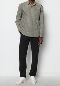 Lichte, gestreepte overhemden in beige en donkergroen, gecombineerd met zwarte broek en witte sneakers. Heeft een klassieke kraag en knoopsluitingen.