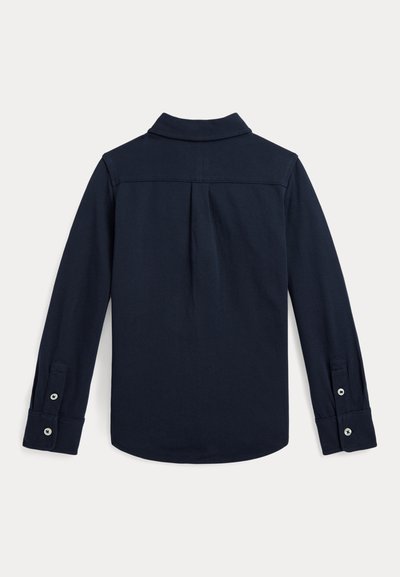 Chemise bleu foncé à manches longues avec col, pli sous le yoke au dos et poignets boutonnés sur un fond clair uni.