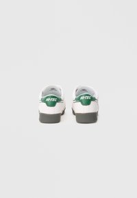 Bijele tenisice sa zelenim detaljima, glatke teksture kože, zaobljenog vrha i sive gumene đonove. Logo "HI-TEC" na peti.