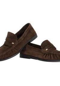 Bruine suede instappers met een gladde textuur, voorzien van een gestikte accent en een klein goudkleurig logo aan de zijkant. Rubberen zolen.