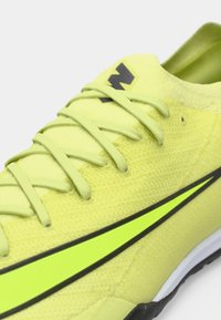 Zblízka na neonovo žltú bežeckú obuv Nike so zodpovedajúcimi šnúrkami a čierne orámovaným logom swoosh na boku.