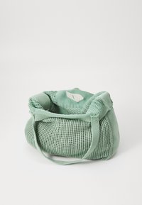 Grüne gestrickte Tasche mit einer weichen Textur, die eine runde Form und einen flachen Tragegurt aufweist. Enthält ein kleines dekoratives Blattsymbol.