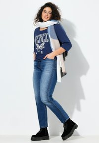 Camiseta gráfica de color azul oscuro con el texto "REBEL", jeans de mezclilla azules con acentos de studs, bufanda ligera en capas y botas de plataforma negras.
