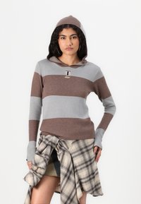 Felpa a righe grigia e marrone, in materiale lavorato a maglia, con cappuccio, accento del logo e maniche aderenti. Abbinata a una camicia a quadri annodata in vita.