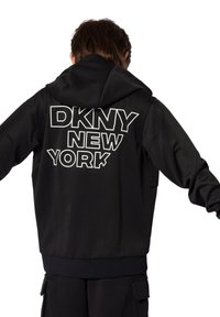 Felpa nera con cappuccio caratterizzata dalla scritta "DKNY NEW YORK" in grande formato bianco sul retro; tessuto testurizzato, vestibilità rilassata e orlo a coste.