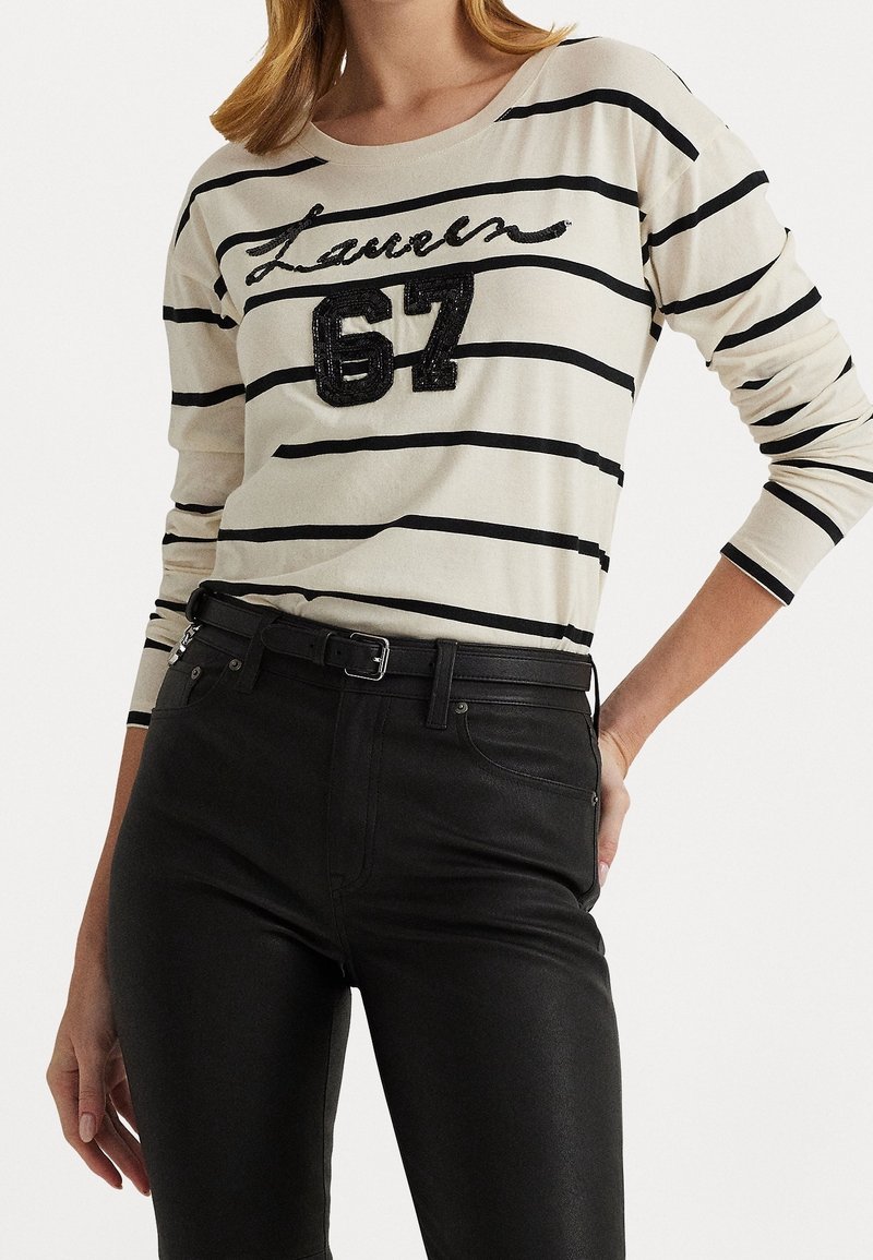 Randig långärmad skjorta i kräm och svart, med en paljettbroderad "Lauren 67" design, tillsammans med tajta svarta byxor och ett svart bälte.