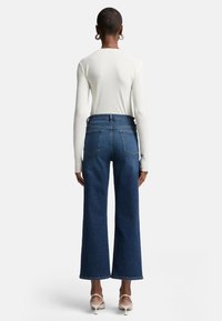 Jeans blu a vita alta e gamba larga con una texture liscia, cinque tasche e orlo grezzo. Abbinati a un top bianco a maniche lunghe.