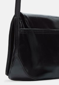 Borsa a mano in pelle nera con finitura lucida, forma rettangolare, cuciture a vista, tasca anteriore e un accento diagonale nell'angolo.