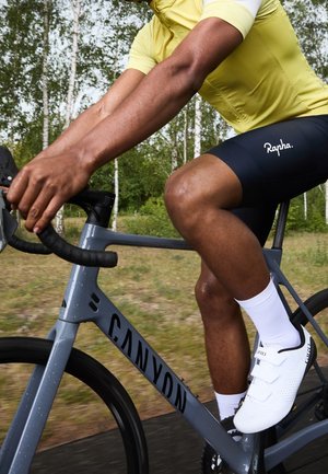 Cycliste portant un maillot jaune et un short noir roule à vélo de route gris Canyon sur un chemin forestier, tenant le guidon et pédalant.