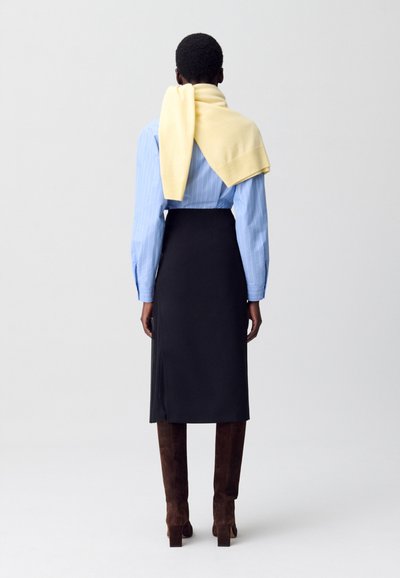 Camicia a maniche lunghe azzurra chiara a righe, sovrapposta a un maglione giallo, abbinata a una gonna nera e stivali marroni fino al ginocchio. Design semplice.