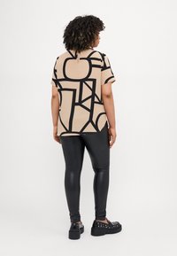 T-shirt beige con audaci motivi geometrici neri, abbinato a leggings neri lucidi e scarpe con platform con dettagli borchiati.