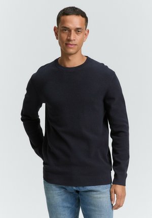 Marineblauwe crewneck trui van een gestructureerde breisel, met lange mouwen en een geribde zoom. Gecombineerd met lichtblauwe denim jeans.