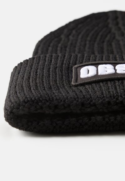 Sort strikket toque med ribbet tekstur, der har en rektangulær lap med hvid tekst og en kontrasterende kant.