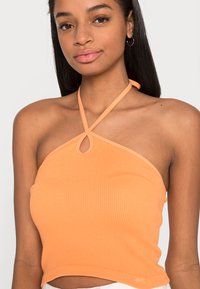 Top em pêssego com textura canelada e decote halter, apresentando uma abertura em forma de olhos na parte da frente e um design justo que acentua a silhueta.