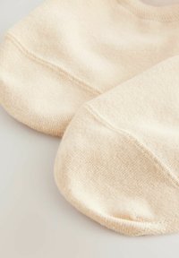 Bež čarape bez vidljivih okica napravljene od mekanog materijala s glatkom teksturom, s zaobljenim oblikom i suptilnim detaljima šavova.