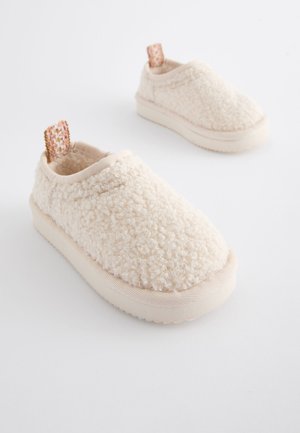 Chaussures sans lacets couleur crème en matériau texturé et duveteux, dotées d'un col rembourré, d'une semelle en caoutchouc beige clair et d'un talon avec un patch à motif.