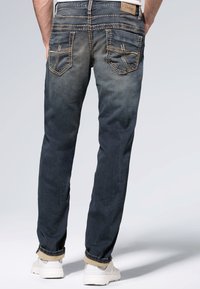 Ciemnoniebieskie dżinsy o przygaszonym kolorze, z tylnymi kieszeniami i starannie wykończonymi szwami oraz brązową metką przy pasie. Regulowane mankiety.