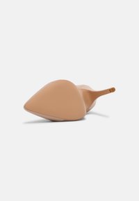 Chaussure à talon haut beige à bout pointu couchée sur le côté, montrant la semelle lisse et le talon aiguille fin sur un fond uni clair.