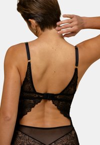 Bralette en dentelle noire avec bretelles réglables, dos ouvert et détails floraux. Comprend un matériel en ton doré et une texture douce et légère.