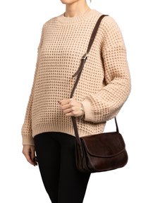 Borsa a tracolla in pelle marrone con pattina, cuciture a contrasto e una lunga tracolla regolabile, abbinata a un maglione beige texturizzato e pantaloni neri.