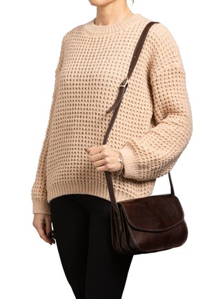 Borsa a tracolla in pelle marrone con pattina, cuciture a contrasto e una lunga tracolla regolabile, abbinata a un maglione beige texturizzato e pantaloni neri.